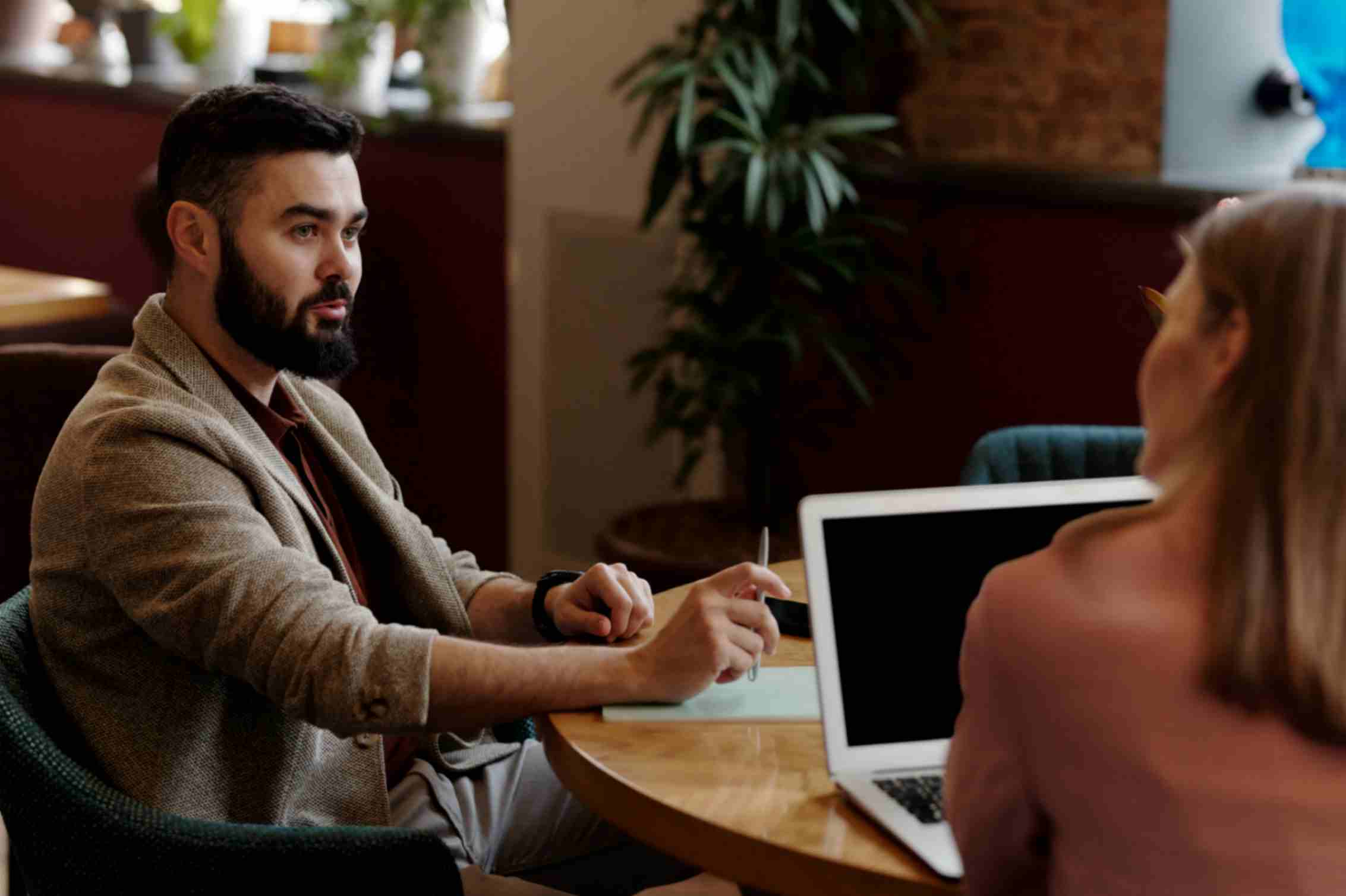 A man and woman seated at a table, using a laptop for a business meeting.