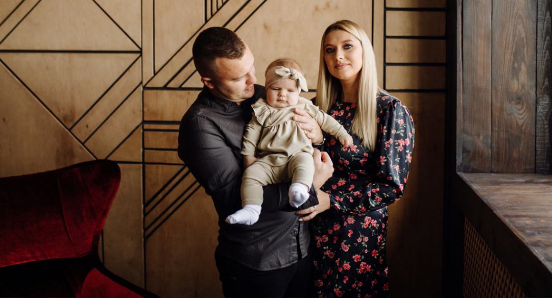 A couple holding their baby in front of a wall.